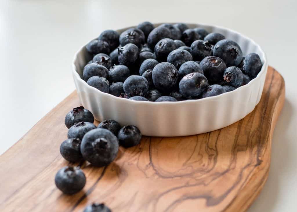 white bowl filled with blueberries on a wooden board
