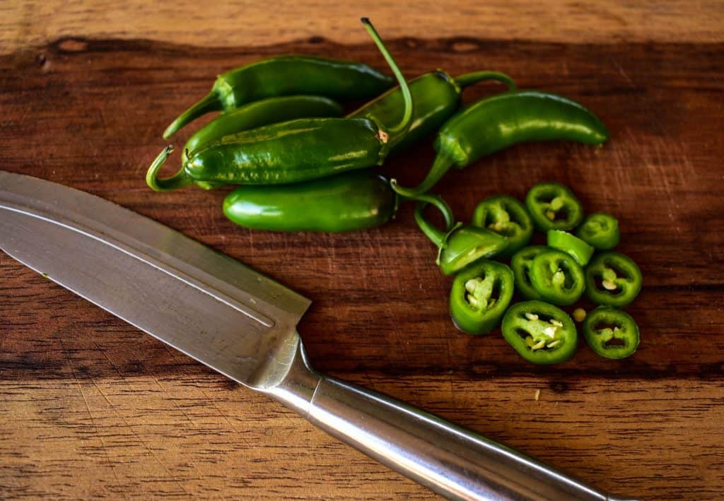 green chopped jalapenos with knife on wooden cutting board
